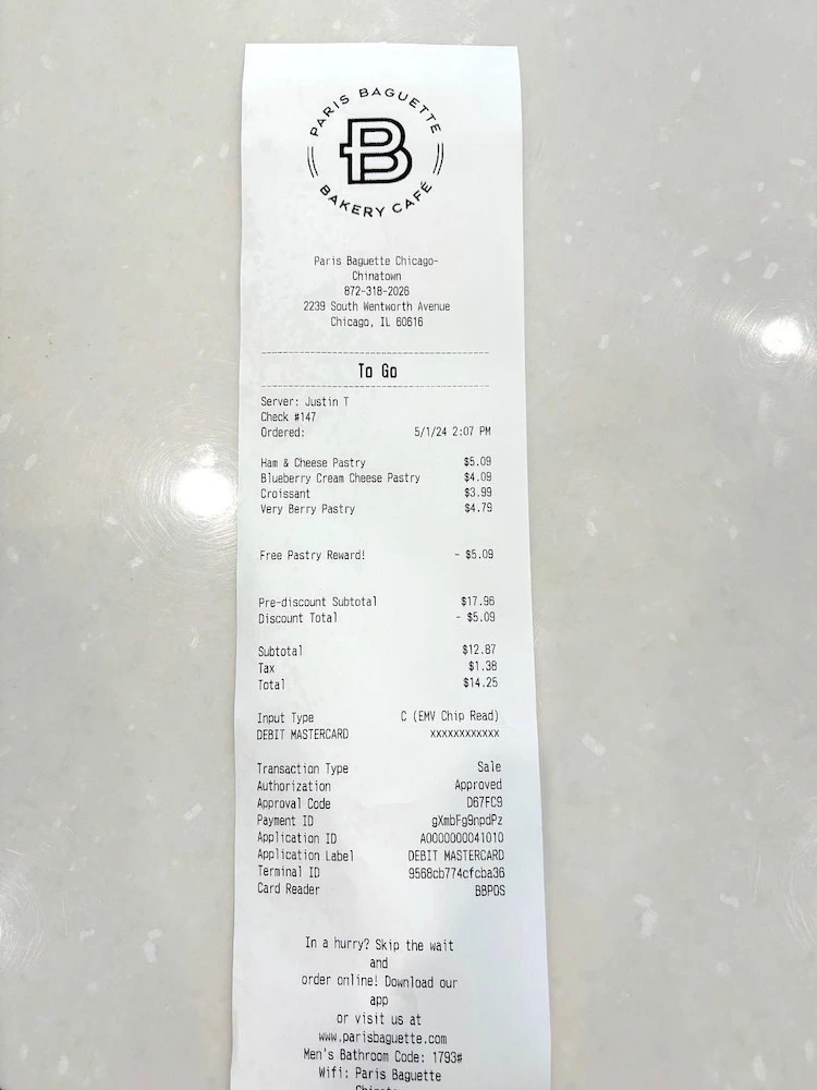 A photo of a receipt from Paris Baguette Bakery Café in Chicago's Chinatown. The receipt details a to-go order served by Justin T on 5/1/24 at 2:07 PM. Items ordered include a Ham & Cheese Pastry ($5.09), a Blueberry Cream Cheese Pastry ($4.09), a Croissant ($3.99), and a Very Berry Pastry ($4.79). A free pastry reward of $5.09 is applied, bringing the pre-discount subtotal to $17.96 and the discount total to $5.09. The subtotal is $12.87, with $1.38 tax, totaling $14.25. Payment was made using a DEBIT MASTERCARD with the last four digits xxxx. The receipt includes transaction details such as authorization code D67FC9 and payment ID qXnbF9npdP2. The bottom of the receipt promotes their app and website, with additional information including a men's bathroom code and WiFi details.